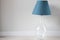 Blue lampshade on the table lamp with glass element near the light wall. Trendy color in your interior