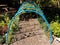 Blue lattice tunnel with netting and plants and mulch path in garden