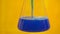 Blue liquid poured into the Erlenmeyer. The liquid flows into the glass bulb. Flask on the yellow background.