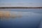 The blue mirrored surface of the lake`s water reflects the stems of the grass standing near the shore. A place to relax