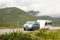 A blue MPV car with a trailer caravan driving on a road in the landscape of Scottish Highlands in misty weather with motion blur