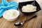 Blue napkin, bowl with sour cream, black bowl with defatted cottage cheese, spoon on wooden table