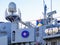 The blue Nato logo on a side of a large gray modern warship with radars and weapons. Naval exercises, attack and defense. Close-up