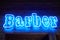 Blue neon wall sing with glowing barber inscription in loft barbershop interior, light strip