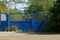 Blue old iron gate overgrown with green vegetation on the street by the road