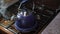 A blue old kettle with a whistle stands on the gas stove, water boils and steam comes from the spout of the teapot.