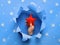 Blue paper flat lay with snowflakes and ripped hole in the middle. Female hand holding soft red star decoration in the hole. Merry