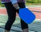 Blue pickleball paddle carried by a female player near the net