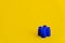 Blue plastic building block on yellow background. Background of plastic detail building block. Part of bright small spare part for