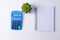 Blue plastic calculator, plant and spiral notebook on white background. Isolate. Isolate. Copy space. Flat lay