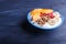 A blue plate with greek yogurt, granola, persimmon, banana, pomegranate on black background