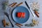 A blue plate with a small gift box next to the cutlery and cinnamon sticks, twigs of Christmas trees and snowflakes.