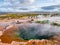 Blue pool with vapour in Haukadalur geothermal area with Strokkur big geyser steam in the background.