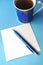 Blue porcelain china cup with blue pen and pencils, white note card and blue background