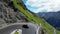 Blue Porsche 911 convertible drives up the hill on Stelvio Pass road a serpentine with mountain alps panorama.
