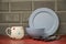 blue pottery china dinner plate bowl with white bone china cup and black handled stainless steel cutlery on a red linoleum work