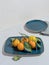 Blue rectangular plate of sweet tangerines with leaves on table