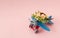 Blue red airplane toy, with pink, red, green bouquet on it, on pastel pink background. minimal romantic concept