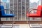 Blue and red waiting chairs against full length window with cityscape in the background