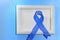 Blue ribbon with white frame on blue background with copy space. Colorectal Cancer Awareness. Colon cancer of older person. World