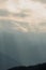 Blue ridge ridge mountain layers with clouds in distance, sun rays shining through, and trees on hills and meadows in foreground