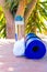 Blue Rolled Yoga Mat Bottle with Water White Towel on Greenery Palm Tree Nature Background. Sunlight. Relaxation Summer Meditation