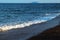 Blue sea over volcanic sand beach. Distant island view. Relaxing sea wave surf over seashore.