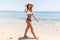Blue sea, white sand paradise. Full length portrait of modern latin woman in bikini and beach straw hat on the seashore walking