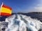 Blue sea of â€‹â€‹ibiza near the coast with traces of the foam lines left by a boat and the spanish flag to the side