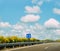 Blue sign pointing up at empty highway with blue sky and fluffly clouds