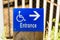 A blue sign on a wooden post featuring wheelchair and arrow indicating the direction to an entrance