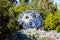 A blue and silver spherical aluminum sculpture in the garden surrounded by lush green plants and trees