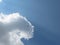 Blue skies with Cumulus white and grey fluffy clouds forming a large shape and a crow flying in the far distance