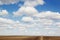 Blue sky background with soft silky clouds, strip field and road.
