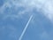 Blue sky with and blurry tiny airplane high up with condensation trails