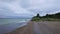 Blue sky, calm sea, white waves, grey sand,and green hill