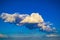 A blue sky with dramatic cumulonimbus clouds framed by silvery cumulus and cirrus clouds scattered across the sky