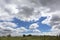 The blue sky emerges through dense clouds over the summer meadow