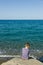 Blue sky and green - blue sea, horizon, silent waves and a little sitting boy can be seen from behind, in foreground coastal rock.