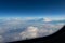 Blue sky in the porthole, white fluffy clouds below. Blue horizon, view from the airplane`s porthole.