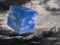 Blue sky and sunshine arriving. Fun weather concept, cube of blue against stormy skies. Surreal image.