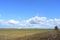 Blue sky. Thick clouds low over the ground. Forest in the distance. Green field of grass. A large field of young grass