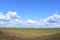 Blue sky. Thick clouds low over the ground. Forest in the distance. Green field of grass. A large plowed field with a tractor