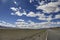 The blue sky and white clouds lead to the next road to the distance. The road is deserted desert