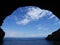 Blue sky with white clouds over sea and cave silhouette