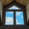 Blue sky and white clouds seen through a large dormer window in a wooden roof