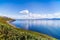 Blue sky with white puffy clouds over rocky coastal line and mountains in a distance