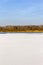 Blue sky, yellow forest in distance, white snowy lake