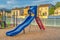 Blue slide with red stairs at a playground against homes mountain and blue sky