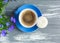 Blue small cup with coffee and macaroon on gray wooden table. Nice summer background with a blue flower in a pot. Spring card